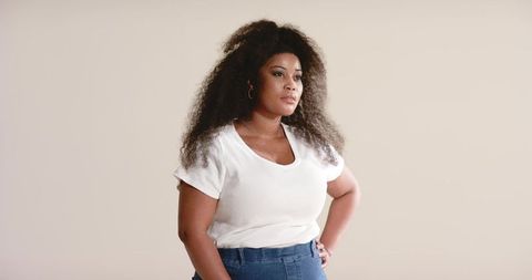 African american woman standing hands-on-hips looking confident in white top and denim