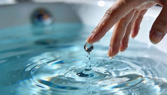 Touching fingertip creating water droplet column and concentric ripples in blue sink basin