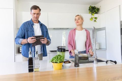 Couple preparing meal at modern bright kitchen island with colander, basil plant