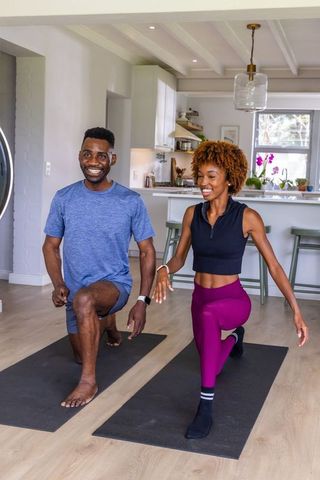 African american couple doing home workout performing forward lunges on yoga mats in modern kitchen