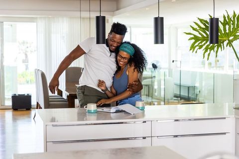 African american couple celebrating while reviewing home paperwork at modern kitchen island