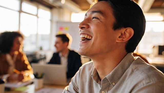 Young professional laughing during collaborative meeting in sunlit open-plan workspace