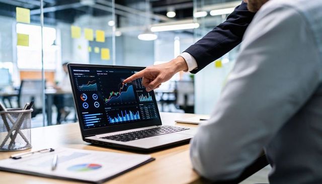 Executive pointing at financial dashboard on laptop while colleague reviewing data in office