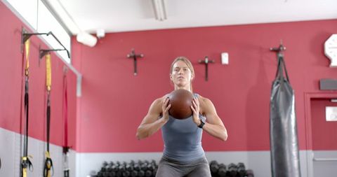 Fit Young Woman Squatting with Medicine Ball in Fitness Center