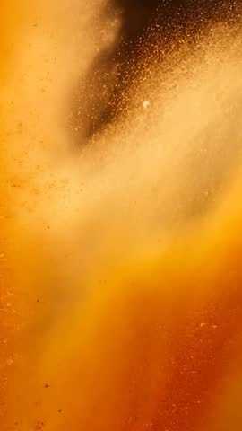 Vertical video of golden powder plume bursting and rising in amber-lit abstract motion