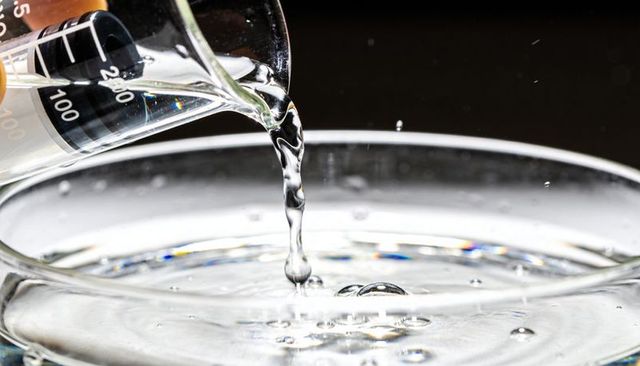 Beaker Pouring Clear Liquid into Glass Dish Creating Splash Crown and Droplets Macro Studio