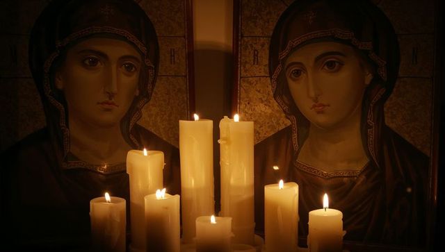 Flickering pillar candles casting warm light on gilded byzantine diptych icons at altar