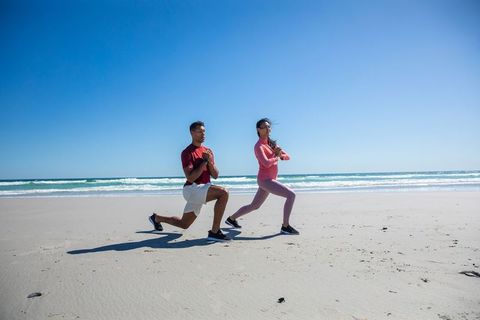 Diverse couple executing lunges on sunny beach