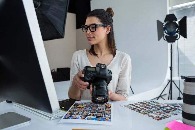 Female photographer examining photos on digital camera at her studio work desk. Ideal for content related to photography professions, creative services, digital photo editing tutorials, camera gear reviews, and behind-the-scenes insights into photography studios.