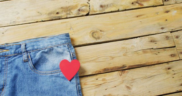 Close up of jeans with red heart on wooden background with copy space. Denim day, material, style and design concept.