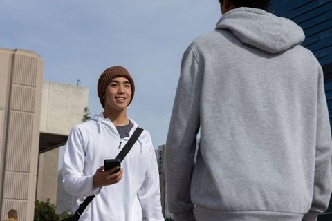Asian man and african american man chatting on campus holding phone wearing beanie