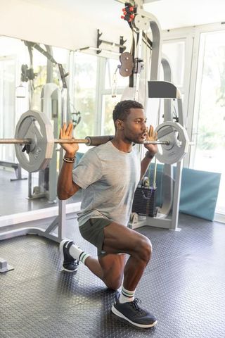 African American man performing barbell lunge in gym for strength and athletic training