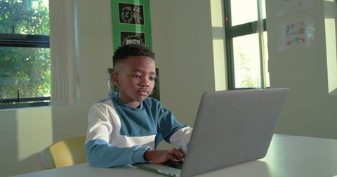 Young african boy studying on laptop in bright classroom natural light focused on online learning