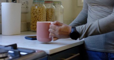 Woman holding pink mug beside smartphone on marble countertop wearing smartwatch and jeans