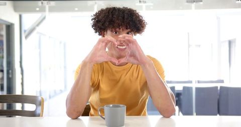 Smiling Man with Coffee Mug Making Heart Gesture at Home