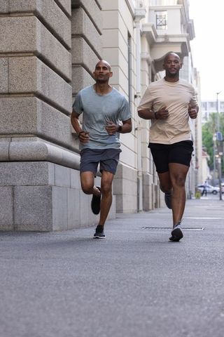 African american male friends running along urban stone building sidewalk for fitness and endurance