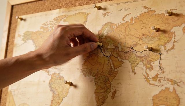 Placing pushpin on vintage world map tracing long route with black cord and thumbtacks