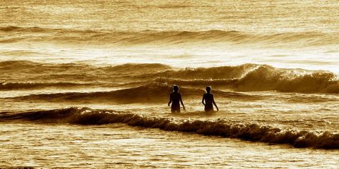Couple wading in golden sea during summer sunset