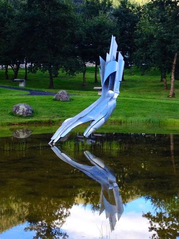 Modern metal sculpture reflecting in pond at outdoor park