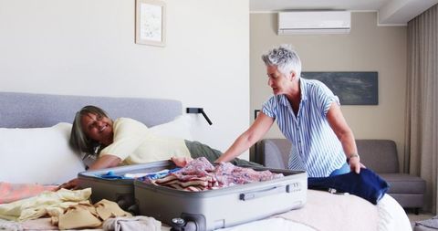 Senior Lesbian Couple Packing Suitcase in Cozy Bedroom for Vacation