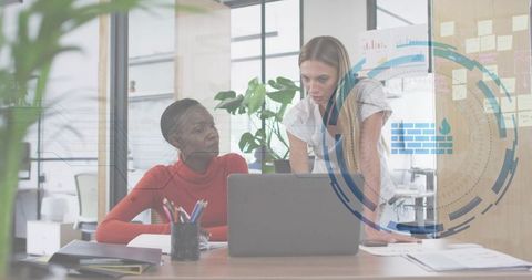 Professional women collaborating over laptop with cybersecurity HUD overlay in office