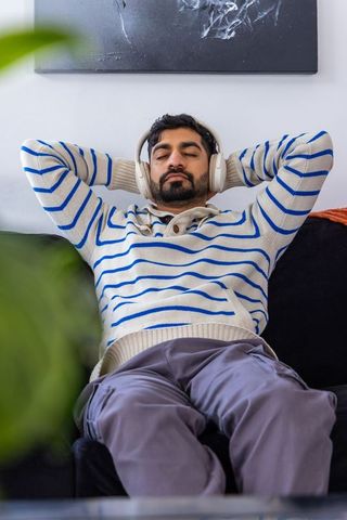 Reclining asian man relaxing with headphones on sofa in cozy modern living space