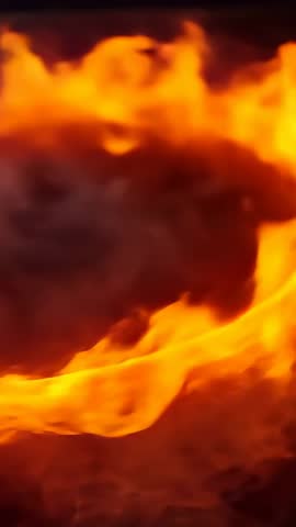 Vertical flame ribbon curling and spiking in close-up over glowing embers, dramatic motion