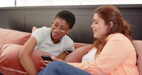 Friends relaxing on coral velvet sofa sharing smartphone and laughing together