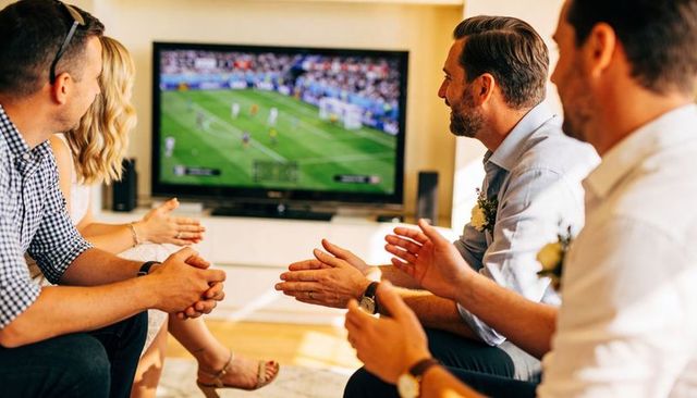 Friends clapping and cheering while watching soccer match on tv during home gathering