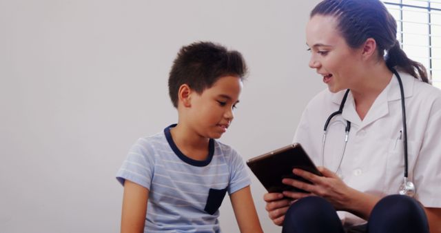 Nurse interacting with young boy using a tablet during a medical consultation, focusing on patient engagement and modern healthcare technology. Suitable for visuals related to healthcare, pediatric care, patient-nurse relationship, and technology in medical settings.