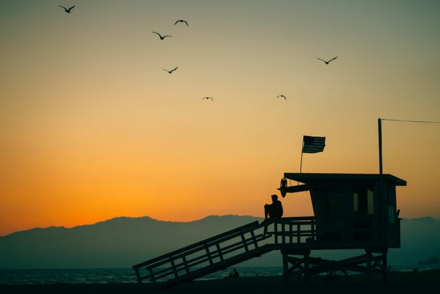 Lifeguard tower overlooking beach at sunset with seagulls flying in sky. Atmospheric scene highlighting tranquility and beauty of nature. Ideal for travel blogs, nature websites, or relaxing wallpapers.
