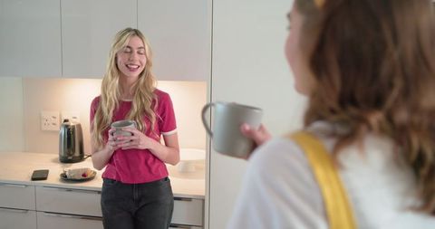 Two friends chatting and sipping coffee in modern kitchen with warm undercabinet light