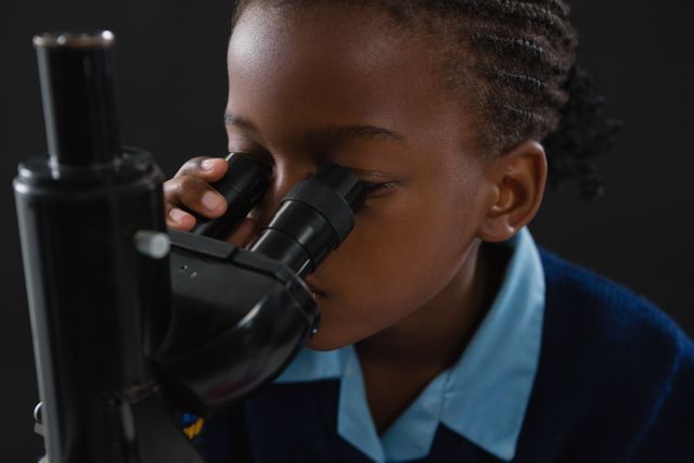 Young schoolgirl intently using a microscope, ideal for educational materials, science and technology promotions, school brochures, and STEM learning resources. Perfect for illustrating concepts of curiosity, research, and hands-on learning in a classroom setting.