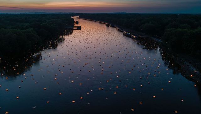 Gliding river carrying floating lanterns at dusk, shoreline reflections and lit boats