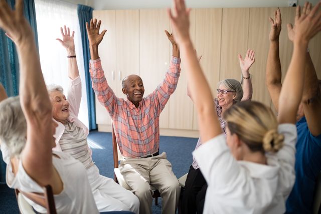 Seniors and a female doctor are sitting in a circle with their hands raised, smiling and enjoying a group activity in a retirement home. This image can be used for promoting senior care services, healthcare programs, community activities, and wellness initiatives for the elderly.