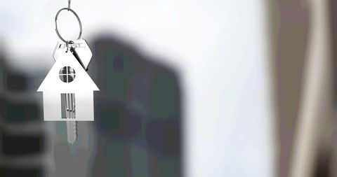 Silver Key with House Keyring Against Blurred Cityscape Background