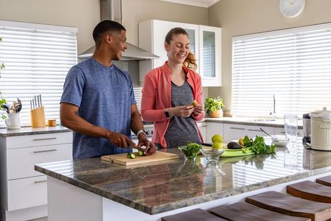 Couple preparing fresh produce on granite kitchen island, smiling while cooking healthy meal
