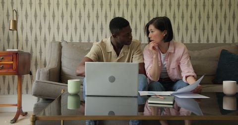 Couple Discussing Finances on Sofa with Laptop and Papers