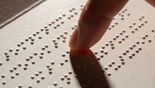 Braille reading fingertip tracing closeup, tactile accessibility concept with shadow