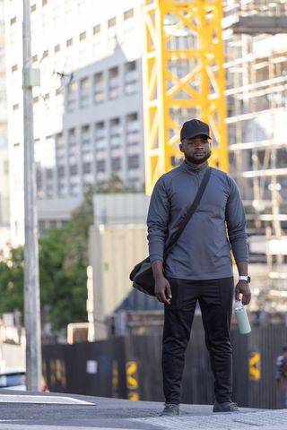 African urban commuter standing by yellow construction crane holding reusable bottle