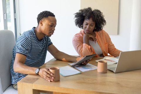 African american couple reviewing budget at home office with tablet, laptop, notebooks