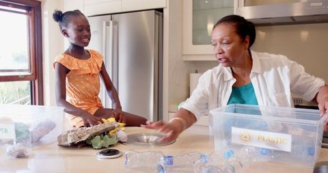 Grandmother and granddaughter sorting recyclables in kitchen