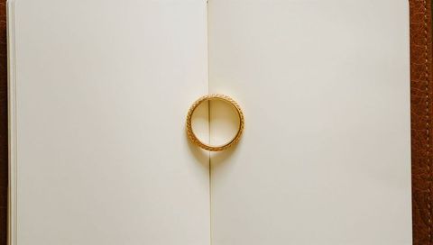 Gold engraved wedding ring casting heart shadow on open notebook spine flatlay