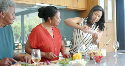 Multigenerational african women preparing salad and pasta together in sunlit modern kitchen