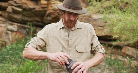 Man in wilderness twisting open container near rock formation