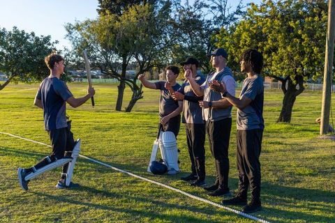 Sunlit outdoor cricket team celebrating returning batsman on park outfield during golden hour
