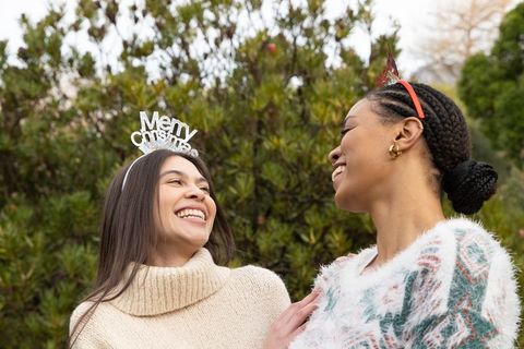 Laughing multicultural friends wearing cozy sweaters and festive headbands outdoors