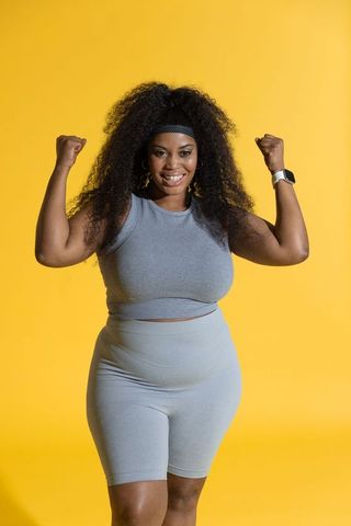 Confident african american woman flexing muscles and smiling in gray activewear
