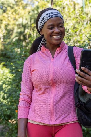 African american woman smiling and taking selfie during park walk wearing pink activewear