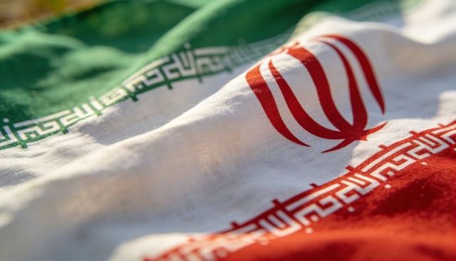 Displaying iranian flag closeup showing red emblem, kufic border and tricolor texture